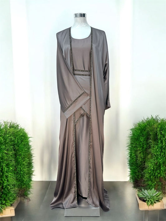 Amara Abaya features a flowing silhouette with a graceful, floor-length design that exudes sophistication. Delicate embellishments outline the edges of the abaya, adding a subtle shimmer and refined contrast to the fabric. The garment includes a matching inner dress, creating a layered effect that enhances its modest yet stylish appeal.