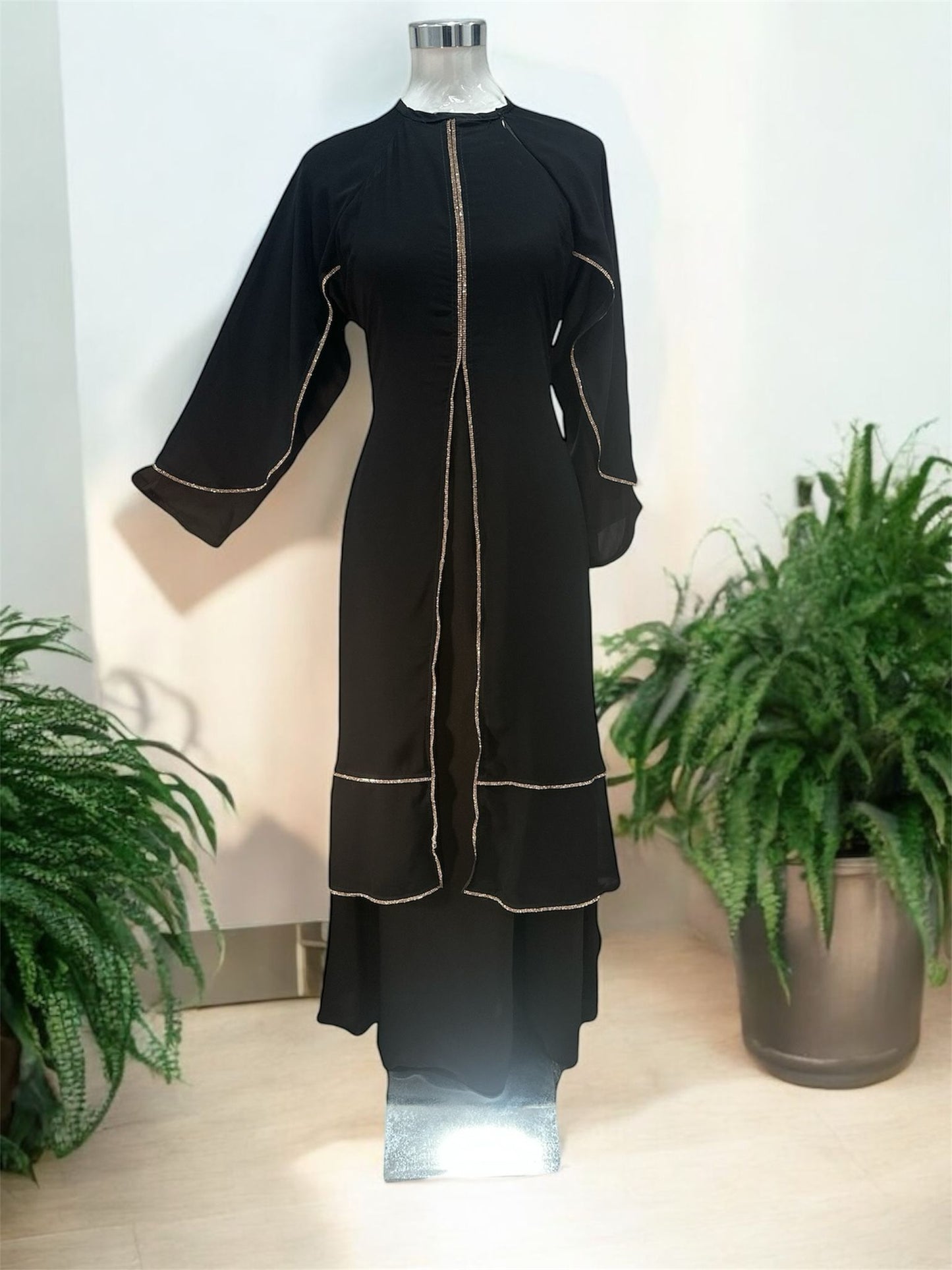 Our Black Riffa Abaya - zip on the left shoulder and is design is with a layered front panel, creating a soft cascading effect that enhances movement while maintaining a polished, modest look. The vertical trim along the center elongates the silhouette, offering a flattering and streamlined appearance.