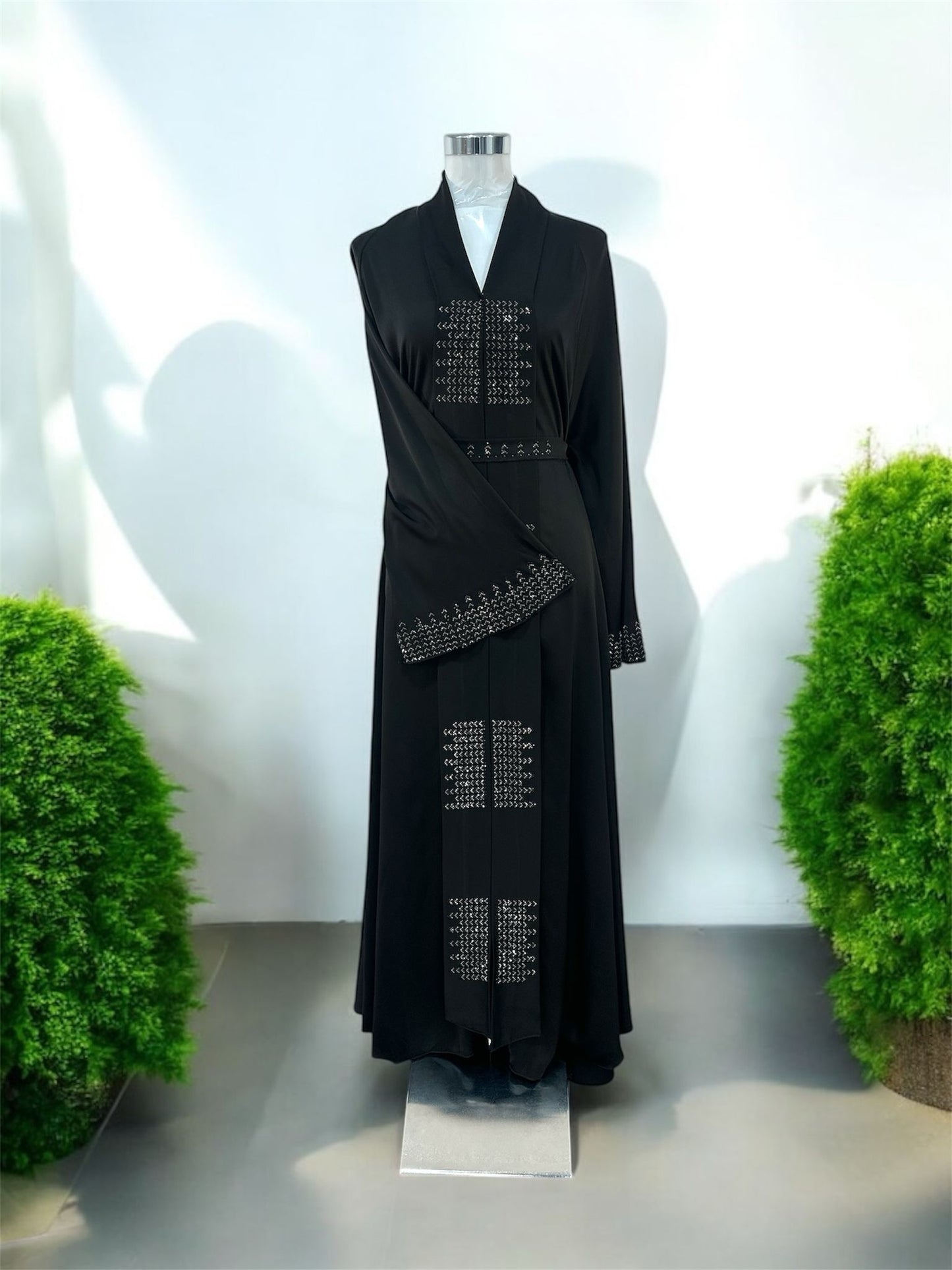 Our Black Riqah Abaya is elevated with intricate embellishment panels placed along the front and cuffs, adding texture and a gentle shimmer while maintaining a minimalist aesthetic. Featuring a structured shawl collar neckline, it brings a sophisticated, tailored touch to a timeless silhouette and a soft draped front overlay enhances movement and creates a layered, graceful effect, giving the piece depth without overwhelming its clean lines.
