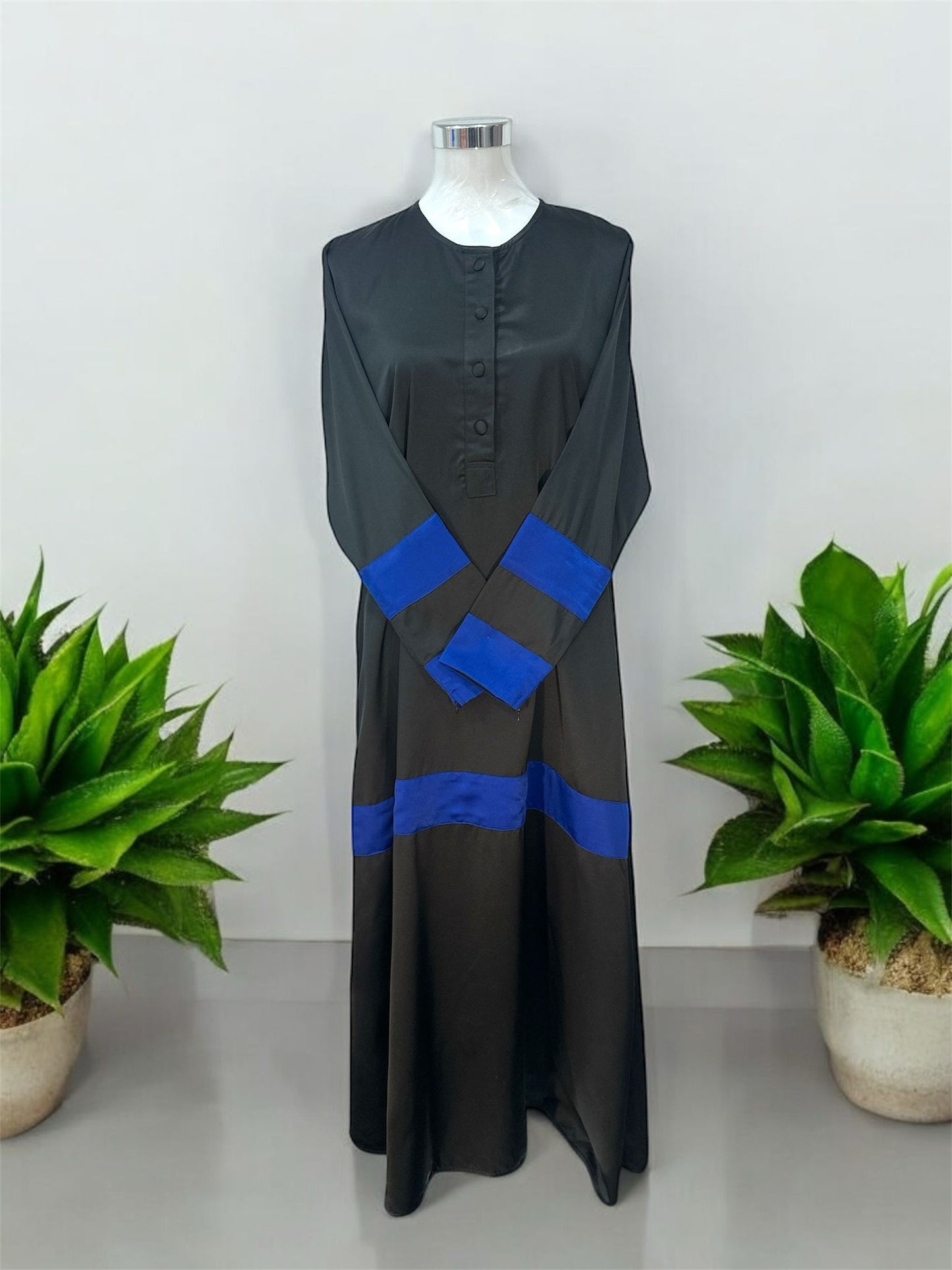 Blue Liniah jubah is tailored in loose, flowy silhouette that drapes beautifully, offering both comfort and sophistication. A round neckline with a buttoned front placket adds subtle structure, while the wide contrast cuffs and matching hem panel create a striking, coordinated look.