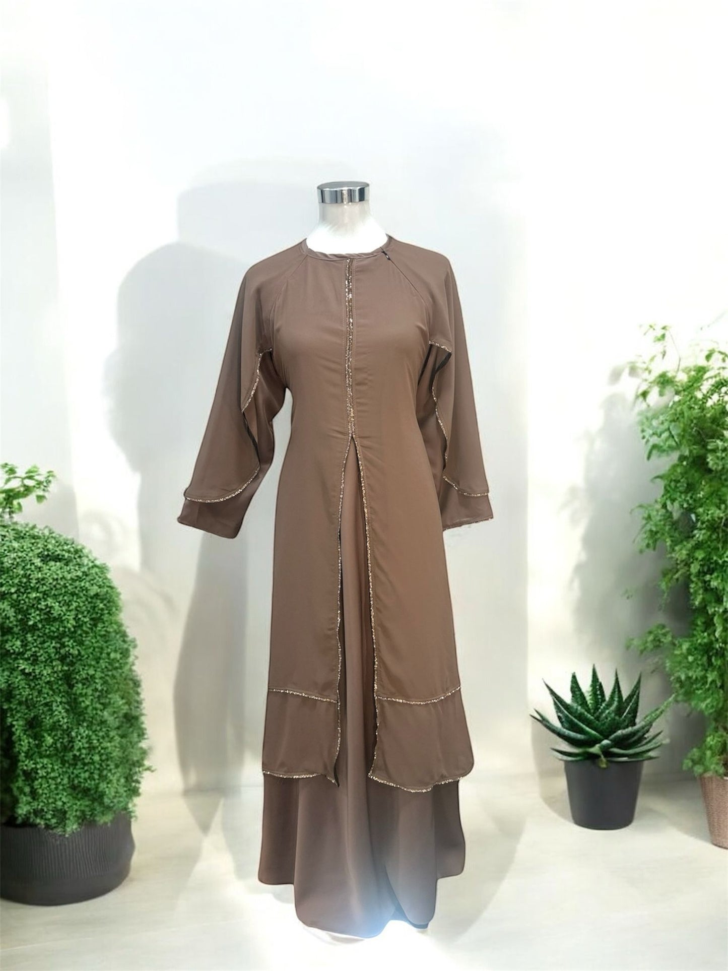 Our Brown Riffa Abaya - zip on the left shoulder and is design is with a layered front panel, creating a soft cascading effect that enhances movement while maintaining a polished, modest look. The vertical trim along the center elongates the silhouette, offering a flattering and streamlined appearance.