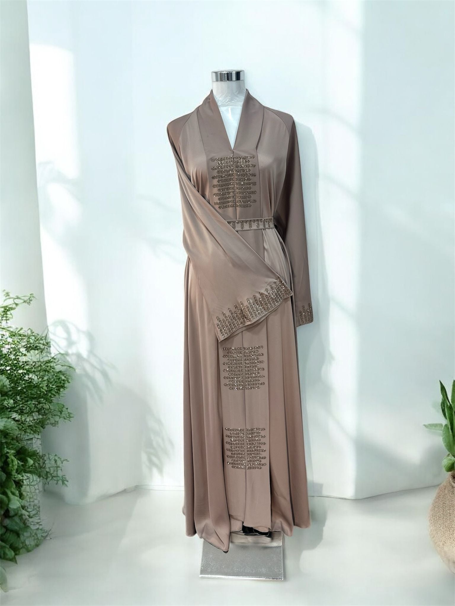 Our Brown Riqah Abaya is elevated with intricate embellishment panels placed along the front and cuffs, adding texture and a gentle shimmer while maintaining a minimalist aesthetic. Featuring a structured shawl collar neckline, it brings a sophisticated, tailored touch to a timeless silhouette and a soft draped front overlay enhances movement and creates a layered, graceful effect, giving the piece depth without overwhelming its clean lines.