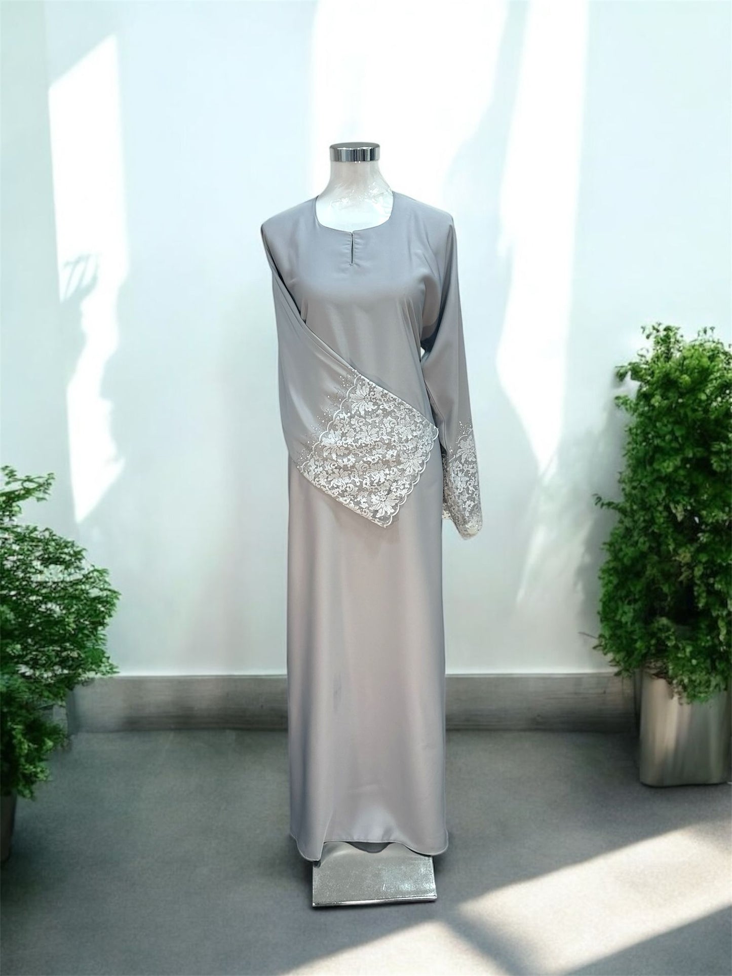 Grey Nisa jubah falls in a clean, elongated line, creating a flattering drape that moves beautifully with every step. A subtle V-notched round neckline adds a modern touch, while the standout feature lies in the delicately crafted lace cuffs—intricately detailed to elevate the overall design with a hint of femininity and refinement and it is paired with a shawl.