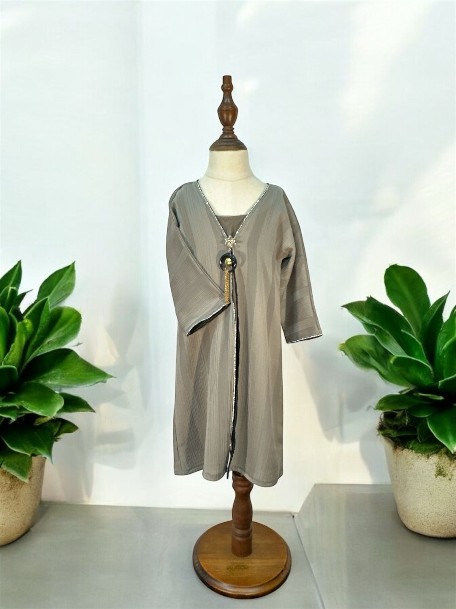Elevate your modest wardrobe with this elegant Ruqi Abaya, designed with a soft textured finish and a graceful flowing silhouette. Featuring delicate embellished trim detailing along the front and cuffs, this piece offers a refined and timeless look. The look is completed with a braided rope belt with tassel accents and a statement pendant detail at the neckline for an added touch of sophistication.