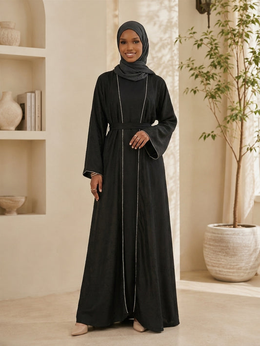 Embrace timeless sophistication with this elegant Amani Abaya, designed with a minimalist silhouette and subtle textured floral detailing throughout. Accented with delicate shimmer trim along the front opening and sleeve edges, this piece offers a refined and graceful look for any occasion. The flowing cut and matching waist belt create a flattering silhouette while maintaining effortless comfort.