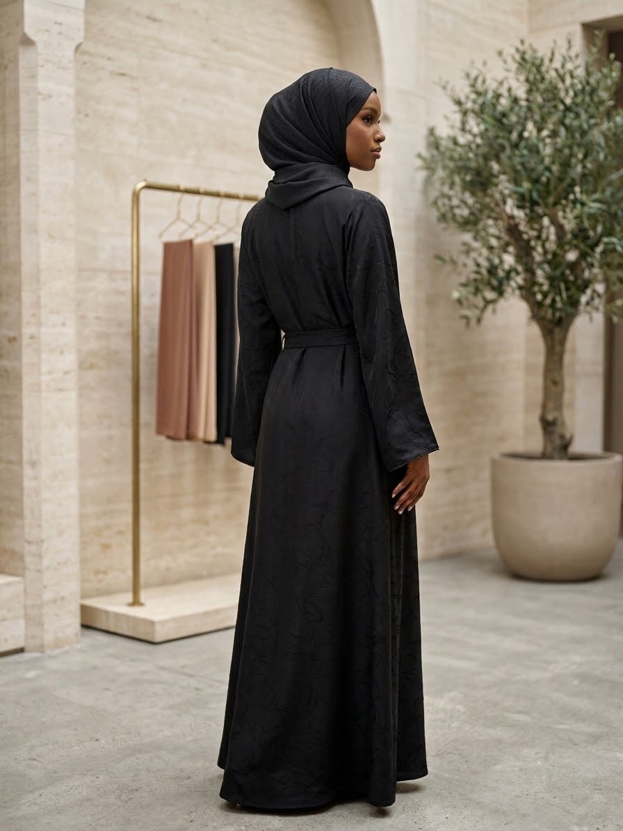 Embrace timeless sophistication with this elegant Amani Abaya, designed with a minimalist silhouette and subtle textured floral detailing throughout. Accented with delicate shimmer trim along the front opening and sleeve edges, this piece offers a refined and graceful look for any occasion. The flowing cut and matching waist belt create a flattering silhouette while maintaining effortless comfort.