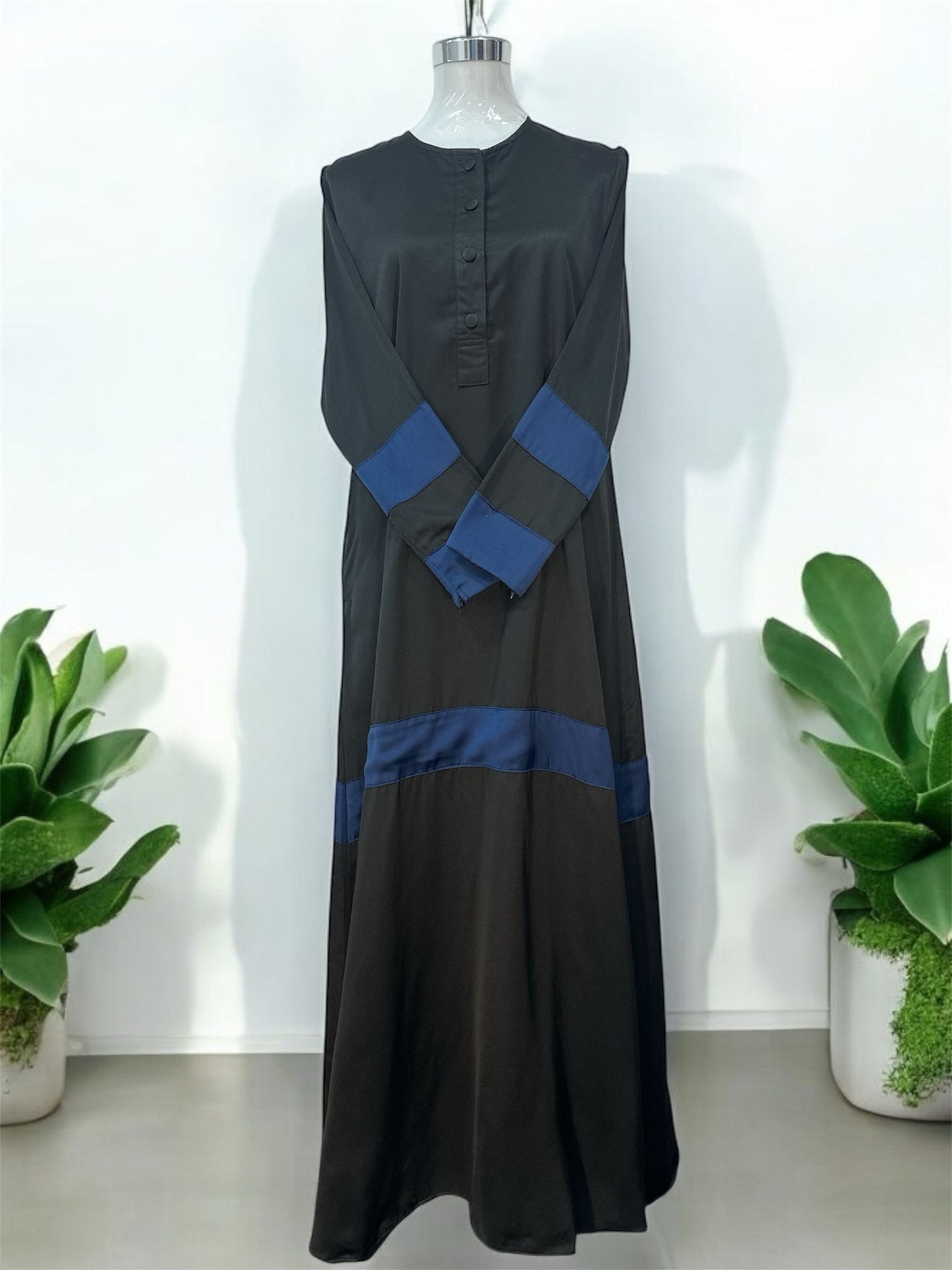 Navy Liniah jubah is tailored in loose, flowy silhouette that drapes beautifully, offering both comfort and sophistication. A round neckline with a buttoned front placket adds subtle structure, while the wide contrast cuffs and matching hem panel create a striking, coordinated look.