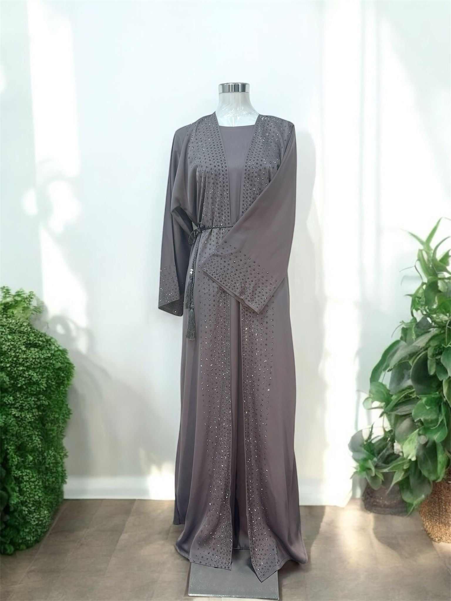 Our Nawra Abaya designed with delicate crystal embellishments that add a subtle touch of sparkle. Featuring a graceful open-front overcoat layered over a matching inner dress, this piece offers a sophisticated and effortlessly modest look.

The flowing silhouette is enhanced with shimmering stone details along the front panels and sleeves, while the matching tassel waist tie adds a refined finishing touch.