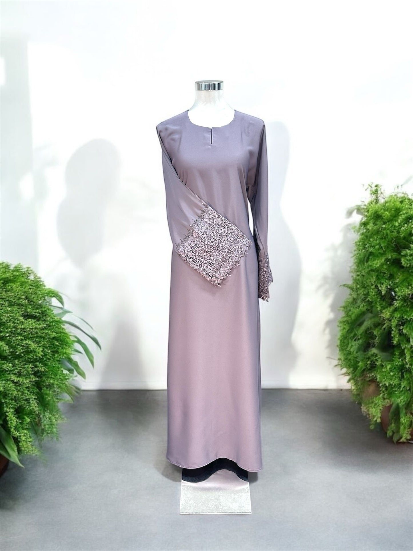 Purple Nisa jubah falls in a clean, elongated line, creating a flattering drape that moves beautifully with every step. A subtle V-notched round neckline adds a modern touch, while the standout feature lies in the delicately crafted lace cuffs—intricately detailed to elevate the overall design with a hint of femininity and refinement and it is paired with a shawl.