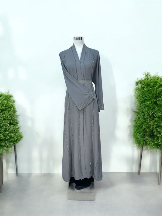 Featuring a structured shawl collar neckline, it brings a polished and sophisticated touch to a beautifully fluid silhouette. Delicate linear embellishments are thoughtfully placed along the front and throughout the skirt, creating a subtle shimmer that enhances movement and elongates the figure.